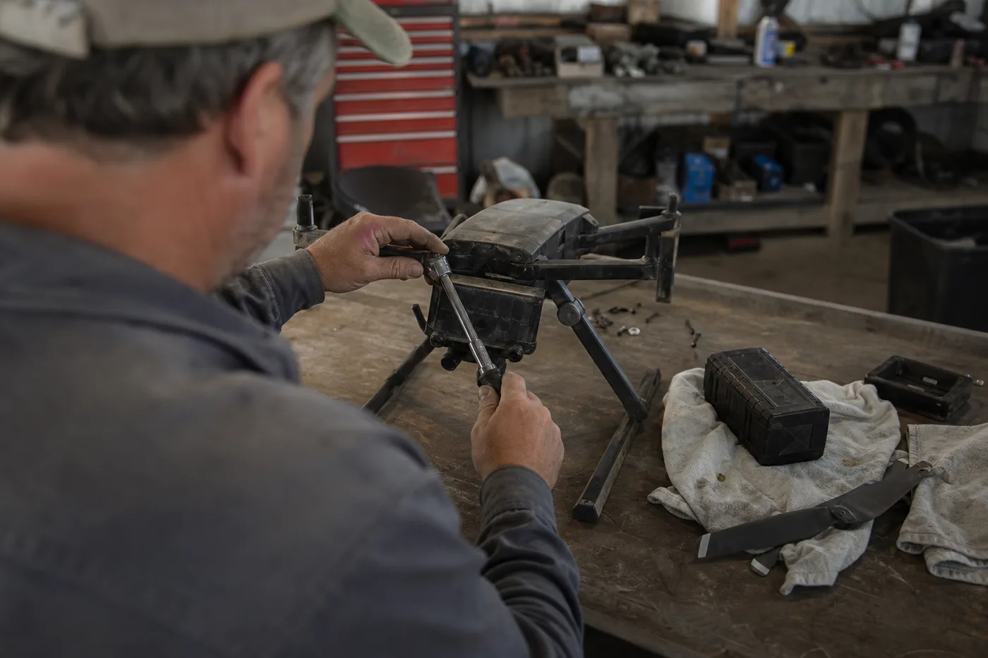 A person in a workshop uses a wrench on a dark drone resting on a wooden table.